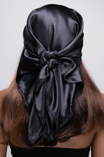 Slender black woman in a black tube top with straight brown hair below her shoulders wearing a shiny, black scarf tied in a knot behind her head.