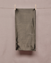 Load image into Gallery viewer, Rectangular, folded, khaki green satin scarf held on a clothesline by two clothespins in front of a light beige background
