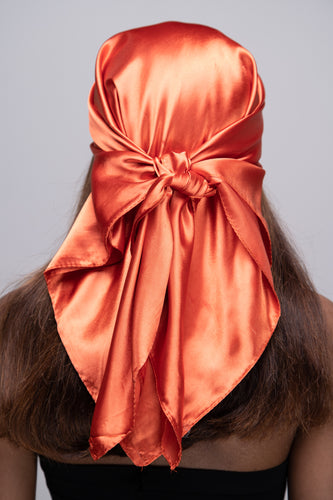 Slender black woman in a black tube top with straight brown hair below her shoulders wearing a shiny, copper colored scarf tied in a knot behind her head.