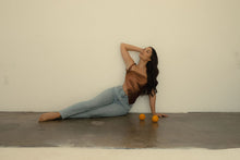 Load image into Gallery viewer, Olive-skinned woman poses in front of a white wall wearing jeans and a chocolate brown satin scarf as a one-shoulder, asymmetrical triangle top. Two oranges lay on the ground in front of her. 
