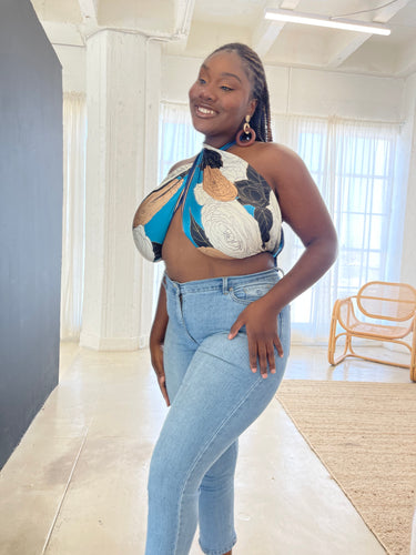 Black woman with cornrows standing 45 degrees to the camera looks at herself wearing jeans and a blue, rose-patterned criss-cross halter top.