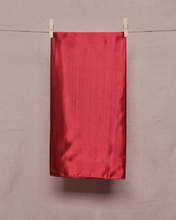 Load image into Gallery viewer, Rectangular, folded, ruby red satin scarf held on a clothesline by two clothespins in front of a light beige background
