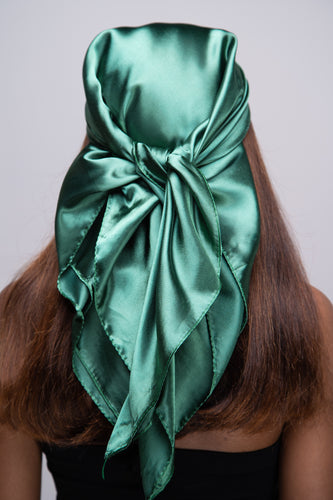 Slender black woman in a black tube top with straight brown hair below her shoulders wearing a shiny, forest green scarf tied in a knot behind her head.