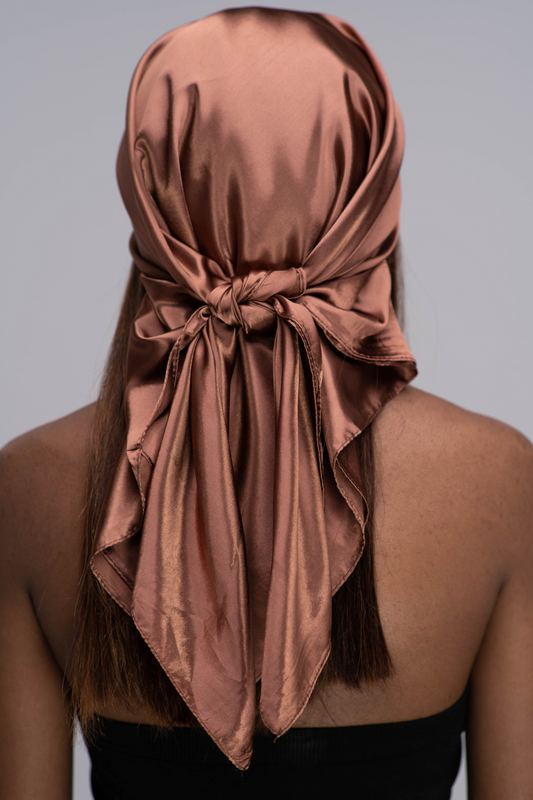 Slender black woman in a black tube top with straight brown hair below her shoulders wearing a shiny, chocolate brown scarf tied in a knot behind her head.